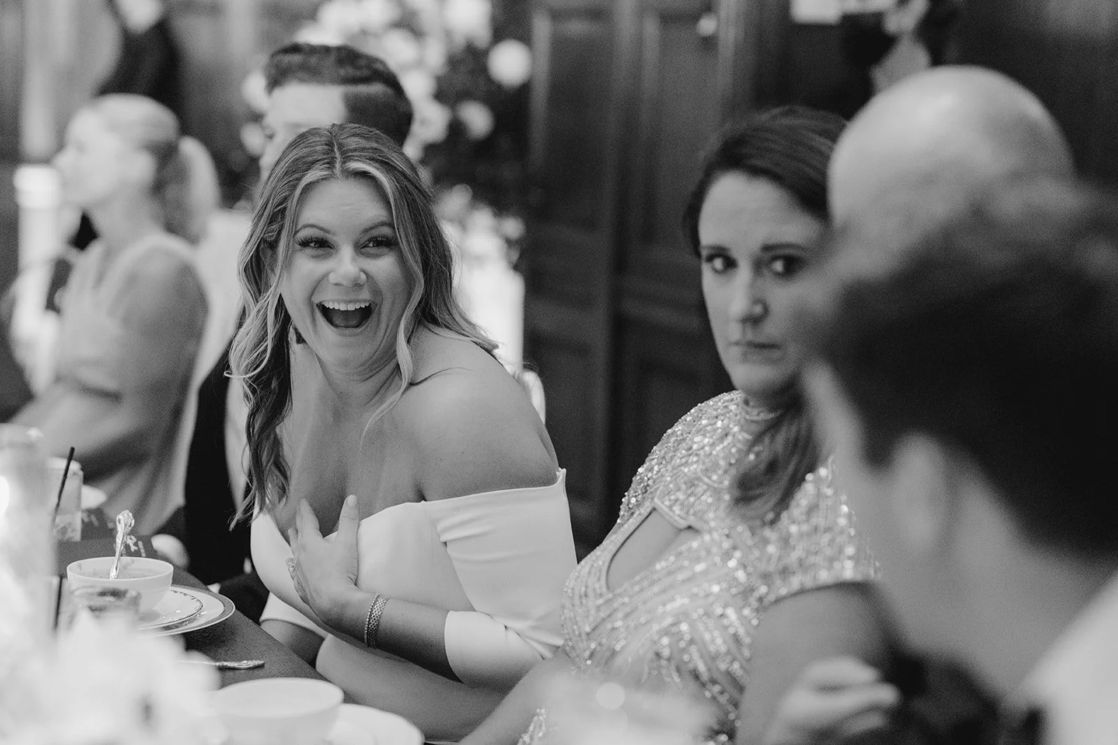 couple relaxed and laughing at their wedding reception while staff work in background